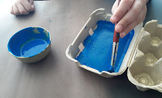 As mãos de um aluno a pintar de azul uma caixa de ovos que será o presépio