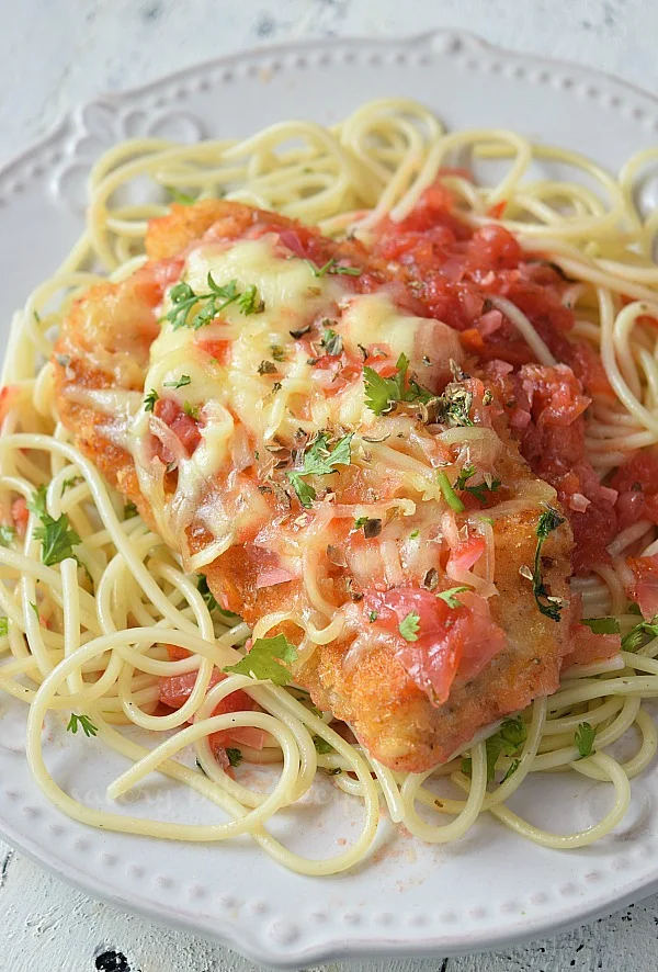 A plate served with delicious and easy crispy chicken parmesan with marinara sauce,mozzarella and served over spaghetti