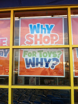 Colorful sign in a store window that appears to read Why shop for toys? Why?