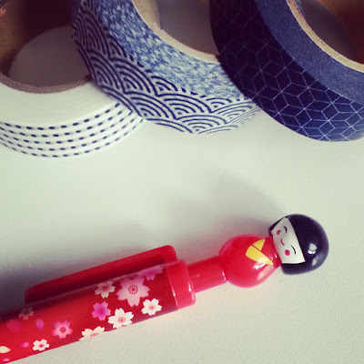 Three rolls of Japanese-patterned blue and white washi tape and a pen with a plastic kokeshi doll on the top of it.
