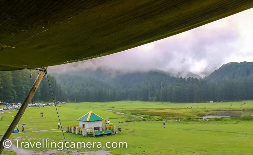 A visit in an year to Khajjiar  has made me click less photographs and rather experience different weather there. I was in Khajjiar during monsoons and this is probably the best season to experience lush green landscapes all around. Khajjiar, at times, is not accessible during winters because roads get closed due to snowfallThis is the first view of Khajjiar lake when you are coming from Dalhousie. This is the point where you should start looking for parking slot. Road condition is usually not very good during monsoons. Maintaining roads in hills is very challenging, but still Himachal has been aggressive in maintaining it's roads. Especially roads in tourist regions.During Monsoons, it's very important to keep umbrella with you, even if sun is shining and there is no patch of clouds. This change in minutes and hence very unpredictable. Our day started with clear sky and by the time we reached Khajjiar it started raining heavily. Fortunately we were carrying few umbrellas and borrowed one from our cab driver.While it was raining, we took a table in one of the restaurants around Khajjiar Lake. It was lunch time and we thought of utilizing this time and had lunch. I am forgetting the name of the place where we had lunch and it was good Punjabi food.A few kilometers ahead there is a temple with this huge Shiva idol. Now let me share a very useful tip. If you came to Khajjiar from Dalhousie in a bus and want to go back in bus only. Reach this place 30 minutes back. Usually there are lot of folks who board bus in Khajjiar and it becomes very challenging to get in. Since this temple is a stop before Khajjiar, there is good probability to get in comfortably and also find a seat. There are 2 buses from Khajjiar to Dalhousie between 1pm to 3pm.So if you come early in the morning, the timings would suit you.These days paragliding  is also quite popular activity around Khajjiar. One flies from a surrounding hill. You need to climb of the hill, so be sure about it. After flight, depending upon the flow of wind you can have a top view of Khajiar, but landing happens in village behind the shiva temple. I haven't done paragliding here so don't know the charges. Bir Billing is best place for Paragliding in Himachal Pradesh and I had that experience.Another view of Shiva from road connecting Khajjiar with ChambaMonsoon is a good time to taste local produce. Local cucumber is much tastier than what we get in cities through cold storage. During Monsoons, you would see lot of folks selling fresh fruit salad around Khajjiar and what can be best snack when travelling in himalayas.Clouds make this place more beautiful. I made some videos of clouds covering this place and going upwards to play in woods, but unfortunately we lost those videos due to card corruption. As I see some herbs vendor in above photograph, so let me warn you about a group of folks who sell you local herbs (don't know what that means and I never bought). But I have heard bad experiences of folks who dealt with these vendors. Please note that most of them are not local folks. and things they sell are not locally produced. They bring stuff from Jammu or Pathankot and sell to tourists. So if you can judge the originality of stuff being sold, go have a talk. Otherwise avoid even talking.  Pre-wedding shoots and post wedding shoots are getting popular in our country. And I noticed lot of couples here at Khajjiar with professional photographers. Some of these photographers roam around the lake and click photographs to hand-over in form of prints. Some of the photographers had come with couples, were indulged in finding appropriate location and guiding these couples for some unique shots.I also wanted to do a shoot with my model, but this time she was acting like celebrities. And even weather was not favoring us. So this time, I couldn't click much.Here is path outside the green meadows, which is used for horse riding. You can hire a horse to have a round of Khajiar or roam around the neighboring villages. I never took the other route where these folks promise to show village and apple orchards.  Carefully notice this photograph. Imagine the view when these clouds are slowing coming out of these forests. This was the best moment and experience at Khajjiar.There are lot vendors selling toys for kids. Urvi also wanted few but settled at one, which didn't reach home safely :). We had long day, so that was expected... I like some of these things at tourist places which provide opportunities for local folks. Some selling these toys, few making fruit salad and others selling juicy bhuttas. And all these things are also available at reasonable costs if you compare with prices quoted in bigger cities like Delhi. And it's not about money, it's more about purity and love of these local folks.This was shot when I was just leaving for Chamba. These colorful baloons in front of these green landscapes looked awesome. Over the years I have seen this place transforming, in good as well as bad ways. Local authorities don't allow people to play any kind of sport on these lawns but there areNames of horses around Khajjiar are very interesting :) ... Romeo, Chetak etc..  If you intend to stay around Khajjiar, there are 3 reasonable options - HPTDC hotel, HPPWD Guest-House and Forest Guest-House. Apart from there are there are various private properties.