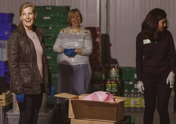 The Countess of Wessex visited the warehouse facility of the Woking Foodbank at Sheerwater. brown coat and pink sweater