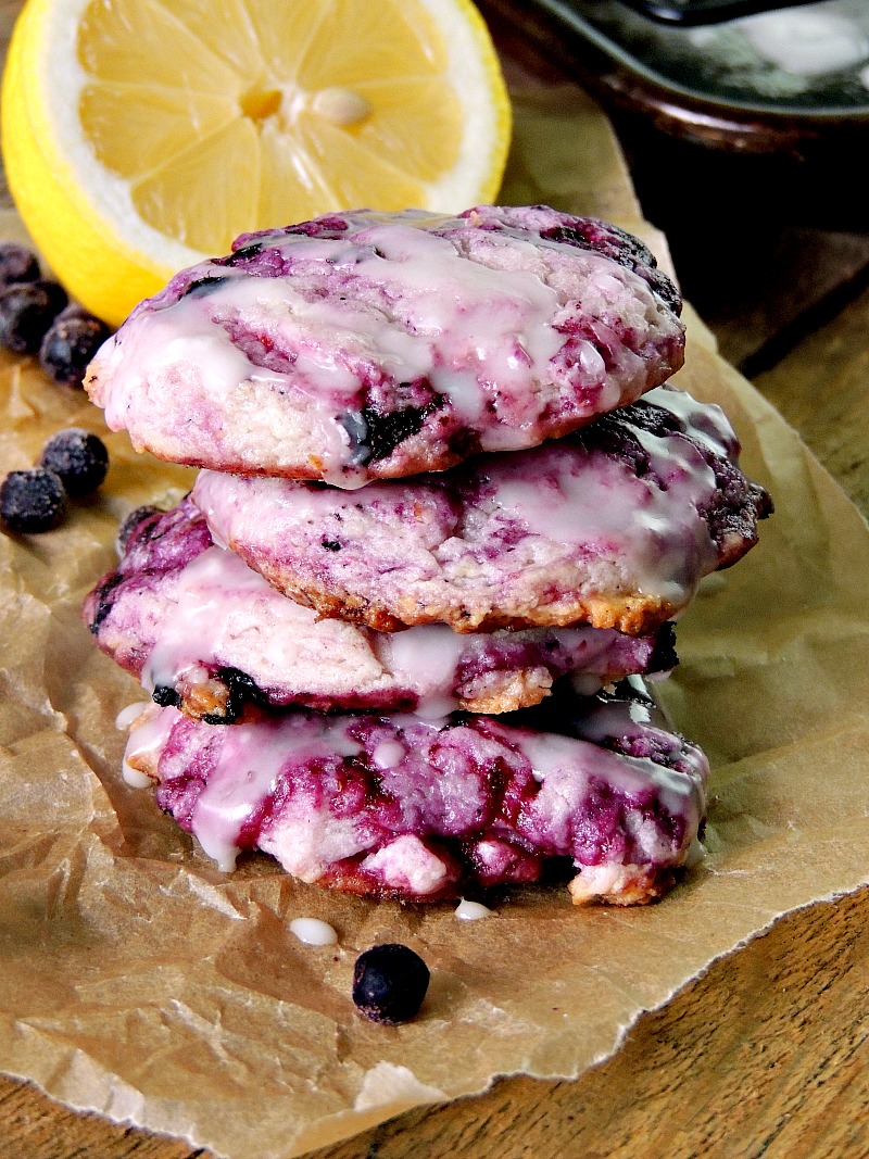Blueberry Cheesecake Cookies with Lemon Glaze on parchment paper with blueberries and lemon in the background