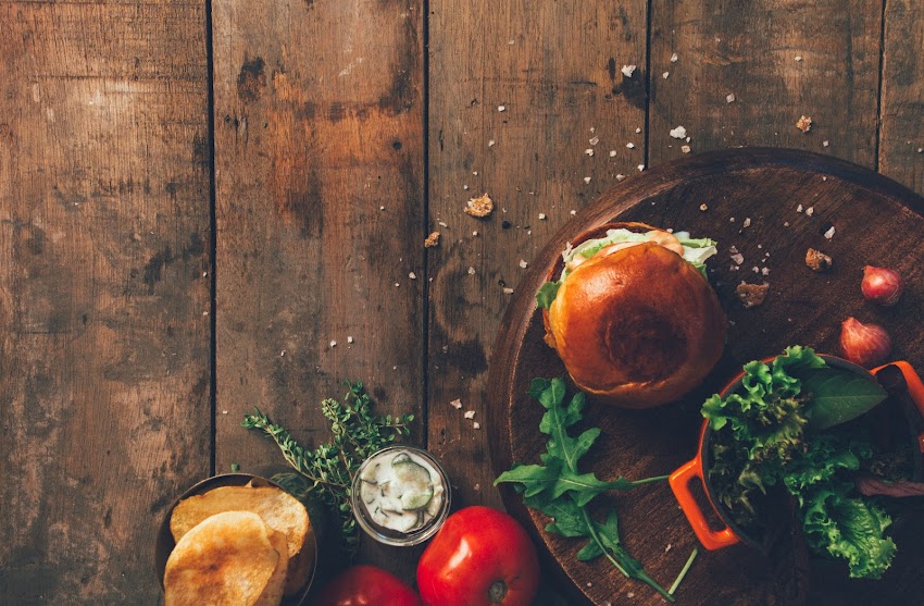 Burger and Vegetables Placed on Brown Wood Surface Burger and Vegetables Placed on Brown Wood Surface