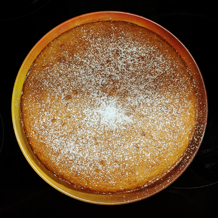 image of a round organge olive oil cake dusted with powedered sugar, sitting on my stovetop