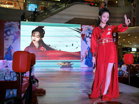female model in red traditional-style dress with only two fingers extended from her raised hand