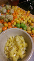 In the forground is a ceramic bowl filled with diced white tomatoes. In the background is a large wooden cutting board covered in white, yellow, and orange tomatoes (as well as a few green tomatilloes).