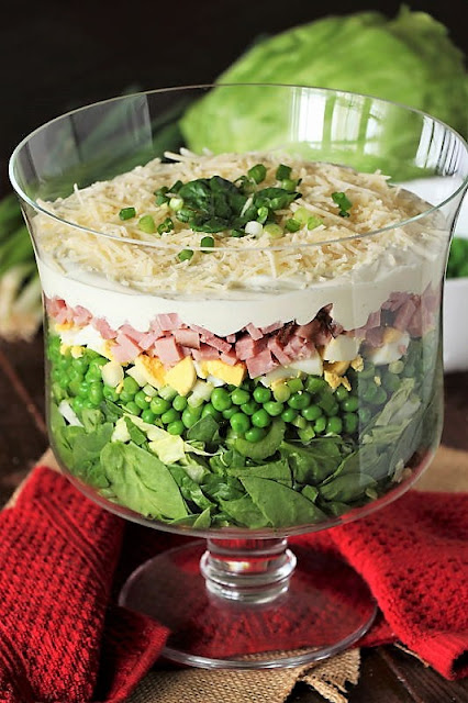 Layered Spinach Salad with Celery, Peas, Hard Boiled Egg, and Ham in a Footed Trifle Bowl Image
