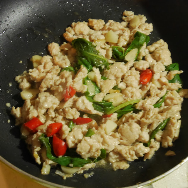 Thai stir fried chicken with red chillies and holy basil cooking in a frying pan