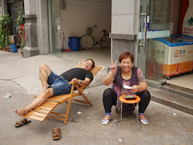 man resting on an outdoor lounge chair and woman posing for a photograph