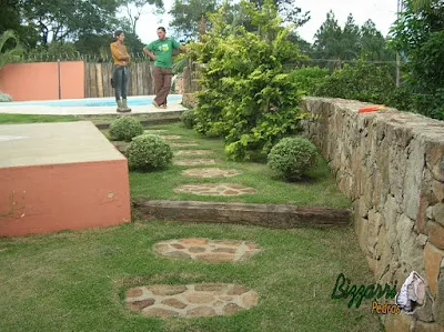 Muro de pedra rústica com os caminhos de pedra no jardim com o degrau de dormente de madeira e a execução do paisagismo em sítio em Mairiporã-SP.