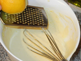 pancake batter in a white bowl with a lemon being zested over it 