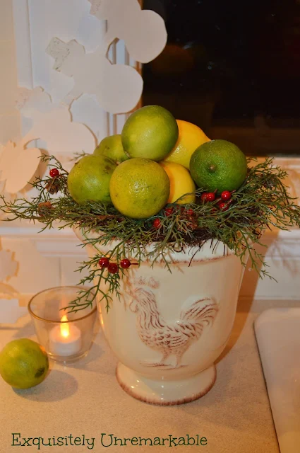 Lemons and limes and evergreen branches in a white crock