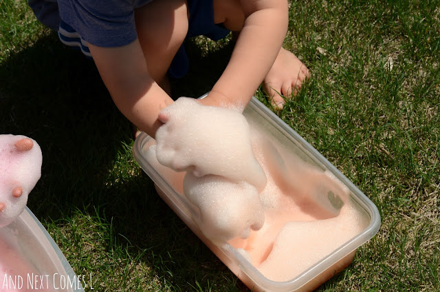 Child playing in an orange sensory bin with colored soap foam