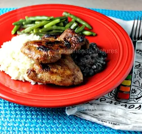 Grilled Jerk Chicken Thighs by Renee's Kitchen Adventures on a red plate with white rice, black beans, and green beans. A fork is next to the red plate. 