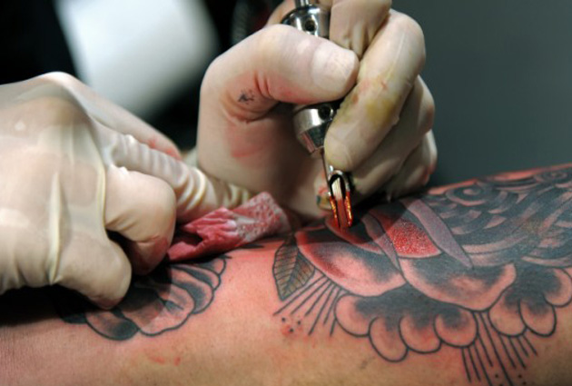 Una mano tatuando, vemos las agujas con tinta roja