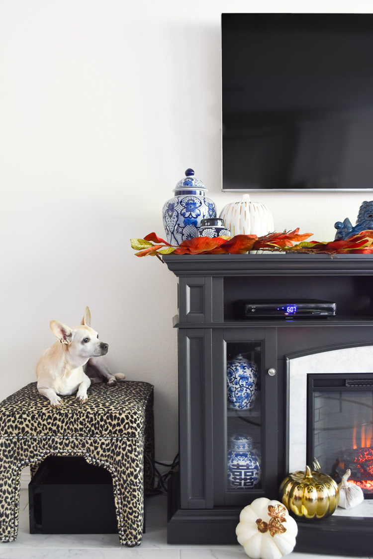 Foo dogs, ginger jars and other blue and white chinoiserie decor paired with white and gold pumpkins on a gray marble fireplace TV stand.