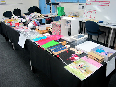 Table in a conference room, covered with piles of crafty items.