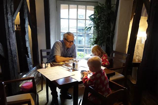 A Dad and 2 children sitting at a table in front of a window surrounded by wooden beams