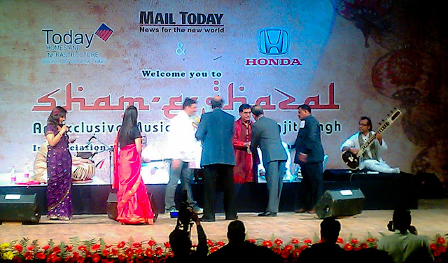 Mobile-giri at Sham-e-Ghazal with Jagjeet singh @ Sirifort Auditorium in Delhi (6th March 2011)  : posted by VJ SHARMA @ www.travellingcamera.com : Finally we got passes for today's Sham-e-Ghazal by Jagjeet Singh. We have been trying to see his live performance for last 6 years but we never managed to get tickets or invitation-Passes. This time, one of my friend arranged few passes for us and we had a lovely evening today ! Although it was but disappointing that cameras were not allowed inside :) ... but thanks to Adobe for gifting HTC Desire HD with nice Camera !!! So this was a good opportunity to try that in very low light conditions... Here are few photographs of Sham-e-Ghazal which are clicked with HTC Desire HD !!!HTC Desire provide various modes of clicking Photographs : Distortion, Vignette, Depth of Field, Sepia, Monochrome, Vintage, Vintage Warm, Vintage Cold, negative, Solarize, Polarize, Aqua !!!Photograph above is clicked using Sepia Mode and it was most suitable for Sham-e-Ghazal :)MAIL TODAY officials presenting flowers to Mr. Jagjeet Singh on his arrival at the stage !!!Mail Today organized Sham-e-Ghazal on 6th March at Sirifort Auditorium and it was planned to start at 6:00 pm... Plan was to close the gates by 5:45 pm and seat availability was on the basis of first come first serve !!! We reached at 5:15 pm and followed the queue.. I mean, started waiting for opening of gate !! There were very few folks at that time and people started coming. At 5:45 pm there were lot of Jagjeet fans in that queue...HONDA Officials presenting flowers to Mr. Jagjeet Singh !!!At 6:00 pm , gates were yet to be opened. It was bit surprising but there were no signs of opening the gates within next 15 mins.. There were two lines initially, one for men and other for women ! After 6:15 pm, few ladies came and started a new line. Other two lines were 300 meter long and people standing at the end started complaining about this third line. Security folks were very lazy and they didn't do anything even when many folks requested them to follow right practices. But no use !! Even people standing in third row were simply ignoring others.. All this didn't impact us because we were in the beginning of first two rows ! Manisha Dube introducing the man who don't need any introduction.. Mr. Jagjeet Singh !!!After standing for 2 hrs in a row, we got entry at 7:00 pm and program started at 7:40 pm !!! It was a great experience listening to Jagjeet Singh in Live show.. btw, we had VIP passes :) So he was very near to our seats !!! Wonderful performance by Jagjeet Singh and his troop of talented musicians !!!If you noticed these photographs, each has different effects and colors :) No editing, all are created in Camera only. HTC Desire HDIt was a good experience and want to Thank the friend who arranged passes for this event & Mail Today !!! But they need to be serious about the security and better planning !!