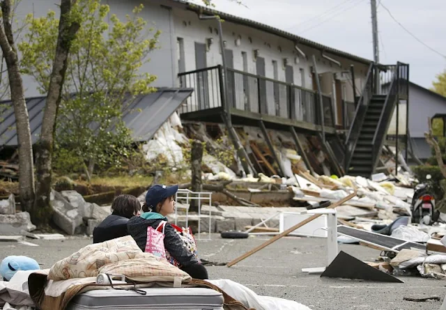  Image Attribute: A university student (R) takes a rest in front of their collapsed apartment caused by earthquakes in Minamiaso town, Kumamoto prefecture, southern Japan, in this photo taken by Kyodo April 16, 2016. Mandatory credit REUTERS/Kyodo