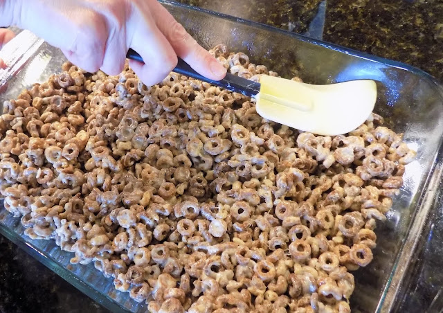 A picture of blended cheerios and melted butter and marshmallows being pressed into a 9 x 13 dish
