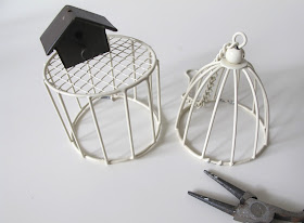 Modern dolls house miniature wire side table, with metal bird cage on top, next to a modern dolls house miniature wire cage-shaped light shade, and a pair of pliers.
