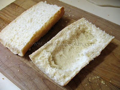 A photo of a French loaf sandwich sliced in half with bread pulled out of the bottom half to make a bowl.