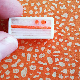 Hand holding an vintage dolls' house miniature plastic radio in front of vintage orange and white paper.