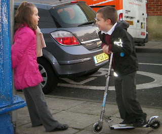 boy on scooter tries to impress schoolgirl in pink coat