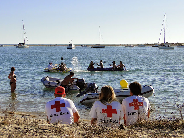 Tres personas sentadas de espaldas de la cruz roja, vigilando a bañistas en la zona recreativa de la playa.