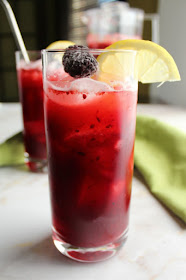 The perfect combination of tart, bright and lightly sweet, this homemade blackberry lemonade is sure to become your favorite warm weather drink. close up glass of dark purple blackberry lemonade with lemon slice and frozen blackberry in joyjolt crystal highball glass