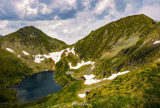  clear lake in mountains with snow and grass on rocky hillside. dramatic weather in picturesque summer scenery