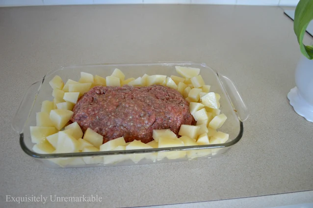 Raw meatloaf and potatoes in a glass dish