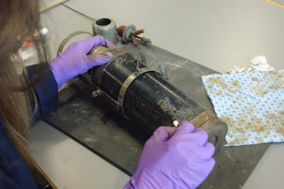 Volunteer Alexandra shown cleaning a piece of medical equipment for exhibition.  Wearing gloves and a lab coat, and using cotton swabs to clean.