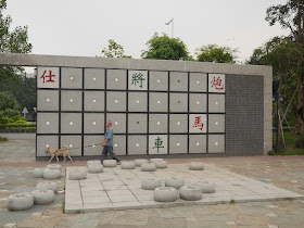 man walking a dog by a xiangqi sculpture at the Dragon Boat Cultural Park (龙舟文化公园) in Zhongshan