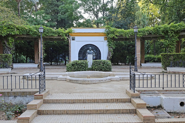 Pequeña plaza en un parque con un estanque y el busto de una persona celebre en el centro como motivo.