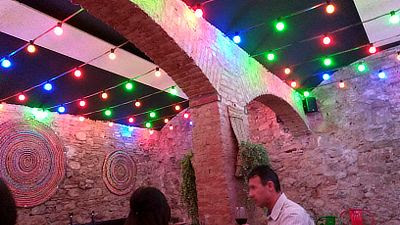 interior de la planta baja del local, en penumbra pero alumbrado en el techo con bombillas de colores. Hay decoraciones mexicanas en las paredes de piedra