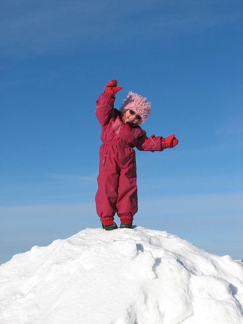 Kind steht im Schneeanzug auf einem Schneeberg