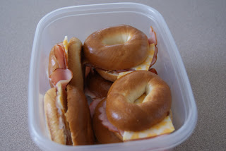 Four ham and cheese bagel sandwiches in a plastic container ready to be put in the fridge.