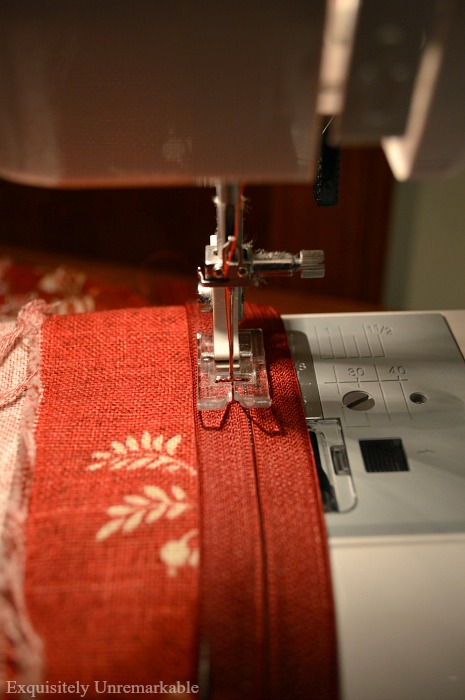 Red pillow cover moving through a sewing machine to attach zipper