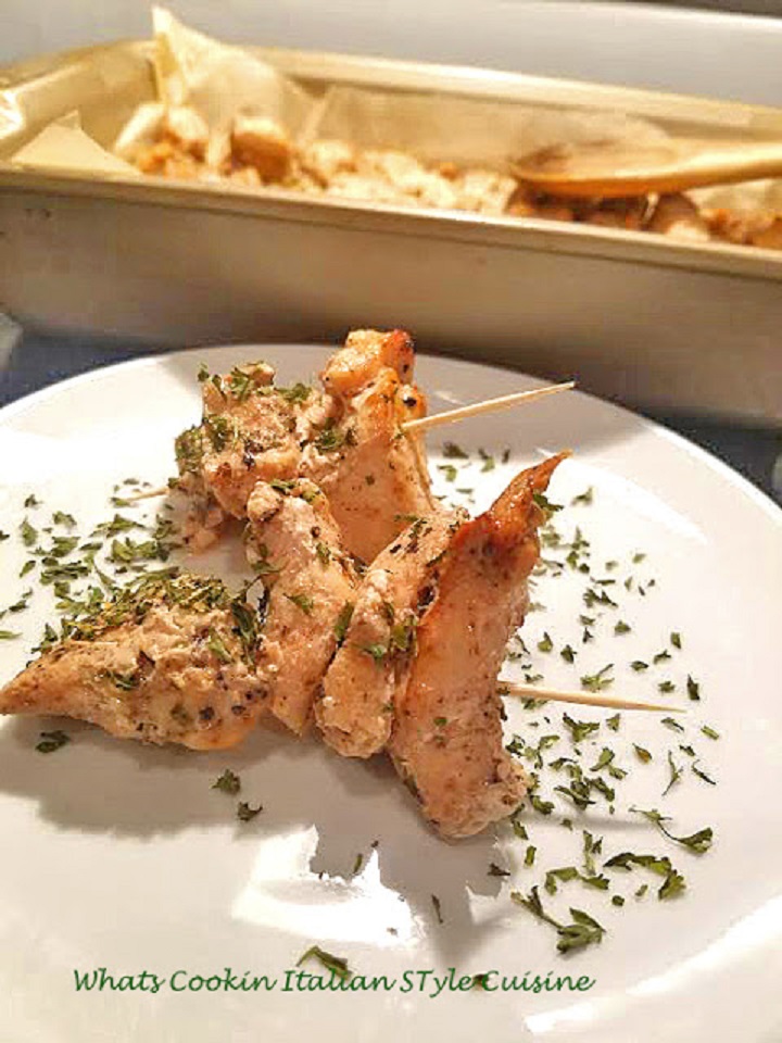 cubed chicken marinated, baked and skewered on a white plate with dried parsley on top