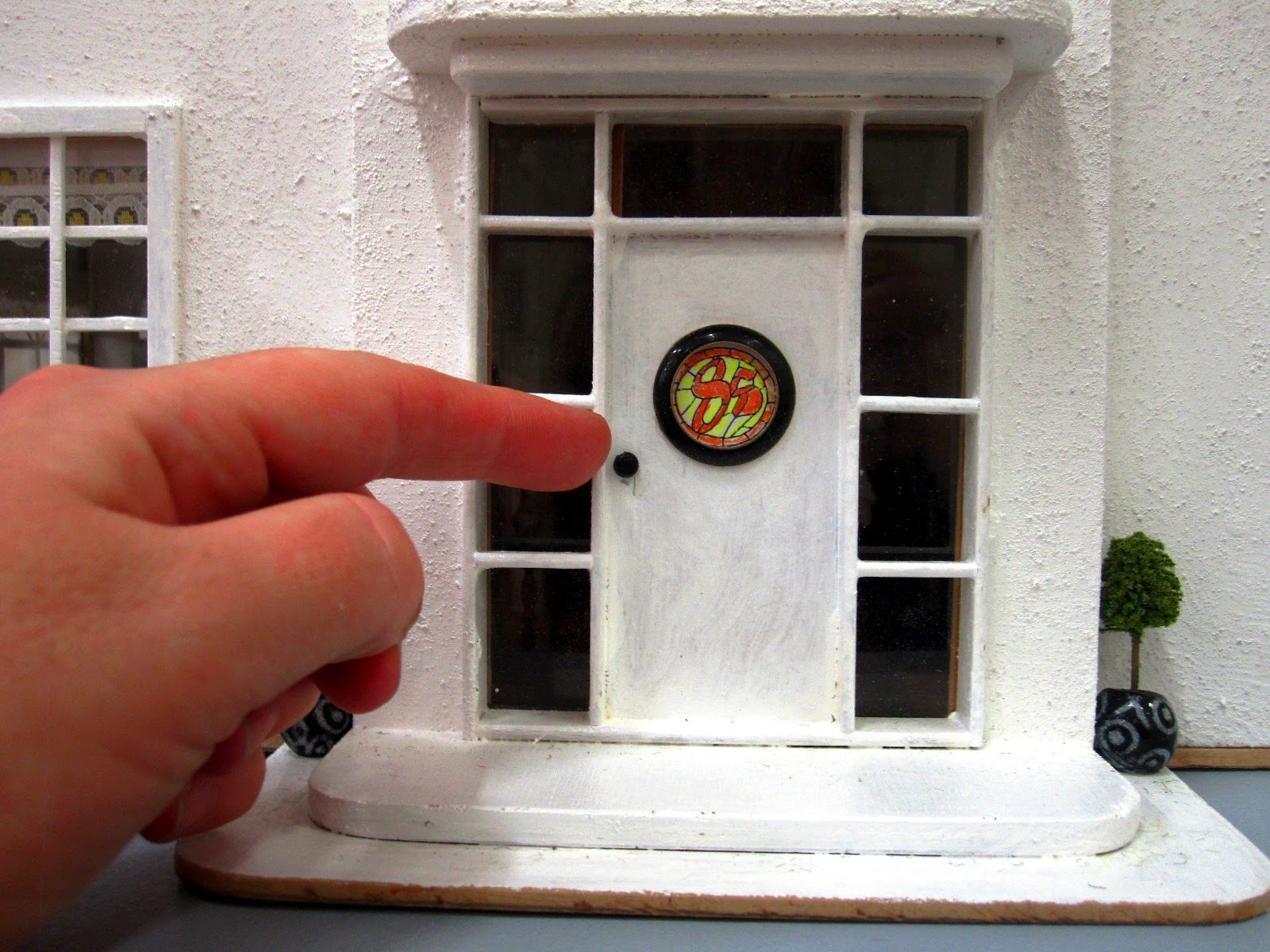 Close-up view of the front door or an Art Deco moderne-style dolls house by Anne Reid, with hand to show the scale of the house (1/24th)