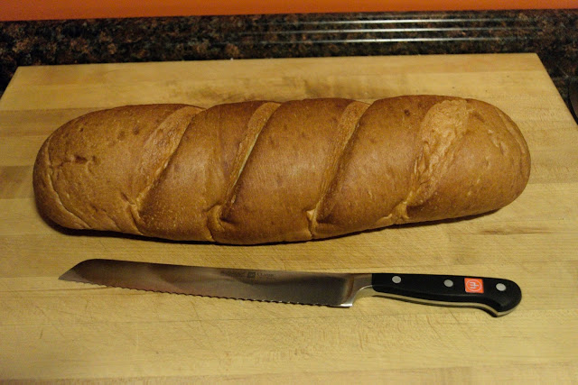 A French Loaf on the cutting board with a  bread knife. 