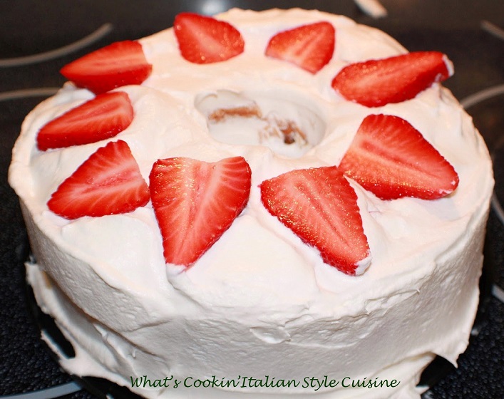 This is an angel food cake with a tunnel inside and filled with strawberry cheesecake filling. This one has heavy cream no sugar and strawberries on top. The cake is on a large plate. This is how to make a tunnel cake filled with cheesecake no sugar pudding, whipped cream and strawberries