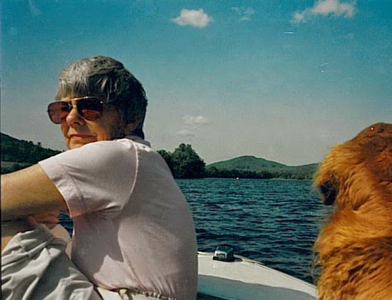 Adult woman in sunglasses, sitting in a motorboat on the water, with golden retriever next to her