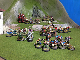 Some miniatures for the Brushfire game arranged on the terrain for a miniatures games. Some examples of the figures include: a badger in a blue uniform wearing claw gloves, a bulldog in a red uniform with a rifle, a chameleon with a crossbow, and a rabbit in teal samurai-style armour.