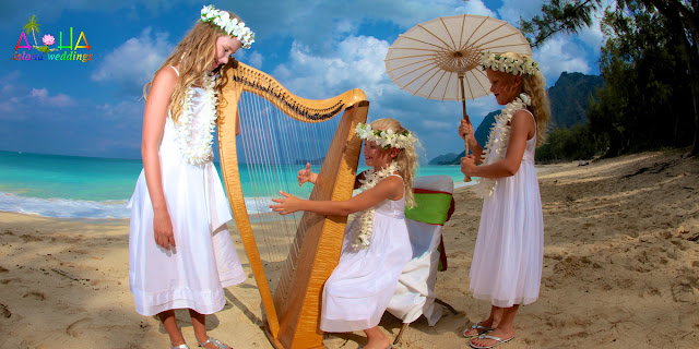 Flowers girls at wedding wearing white crown of of tropical florals play the harp at their moms wedding