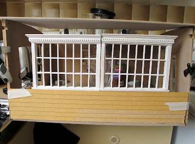 Mock up of a  dlls' house miniautre shed kit, with multipane windows propped up along the front wall.