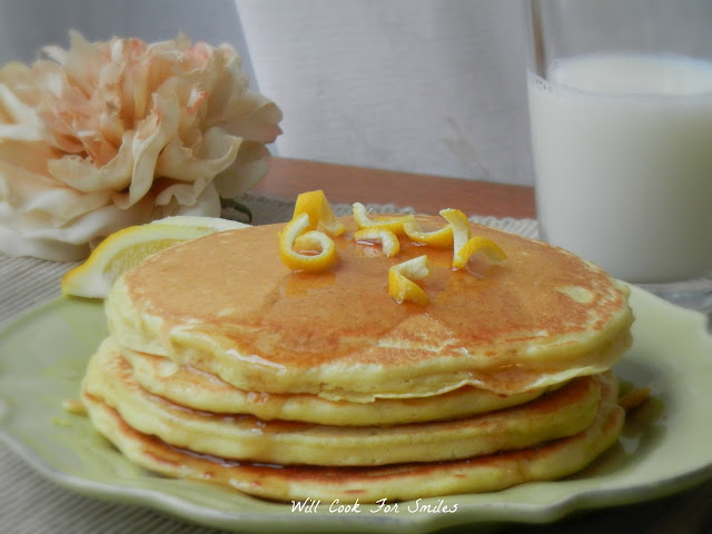 pancakes with lemon zest on top on a green plate with a flower on the left and a glass of milk to the right of the plate 